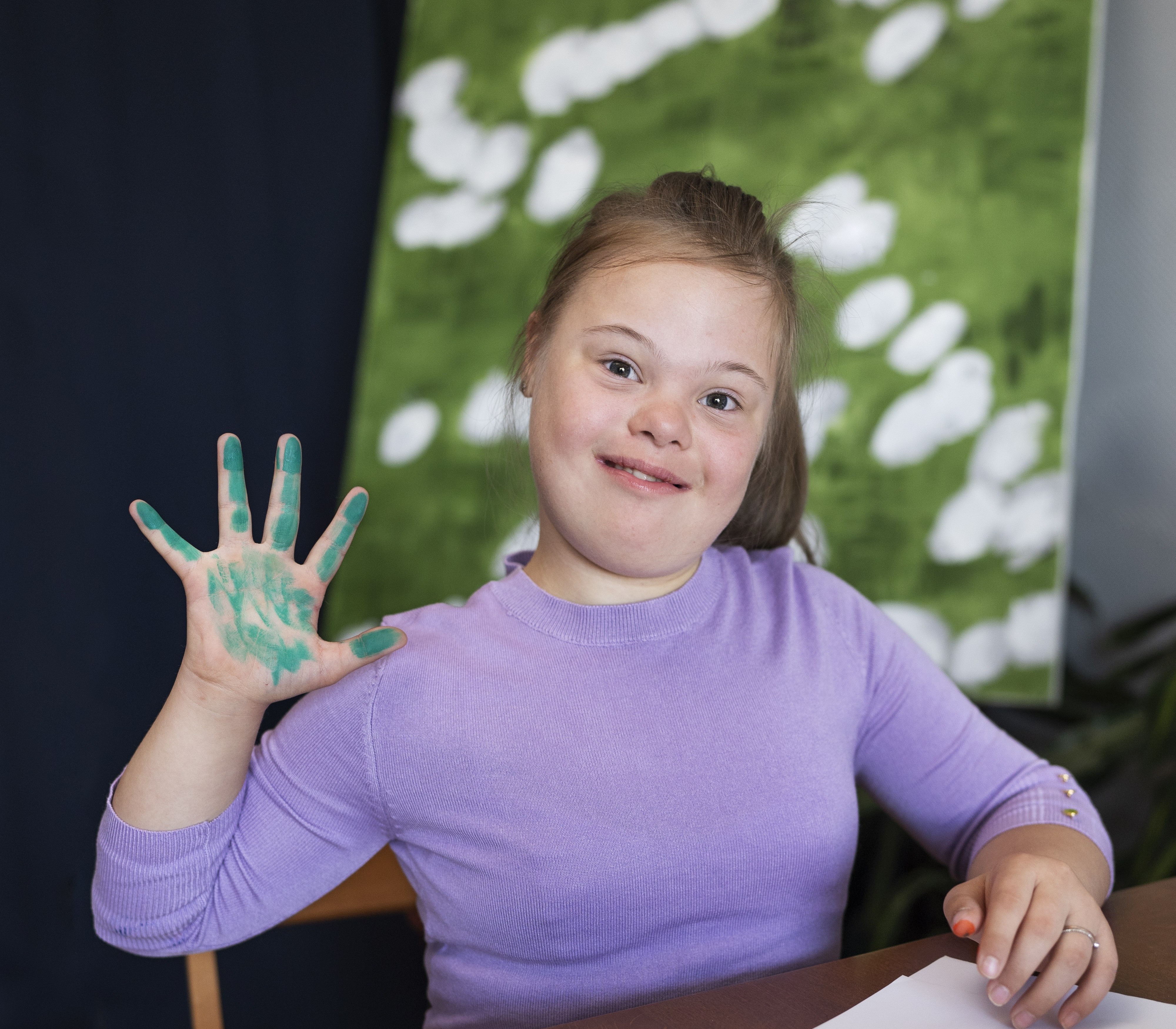 Girl smiling while painting at a table showing her artwork